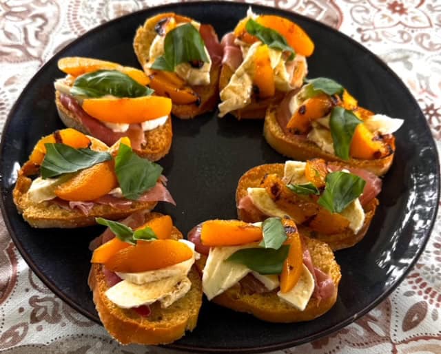 Hapje met vlees, kaas, paprika en basilicum op een zwarte schaal.