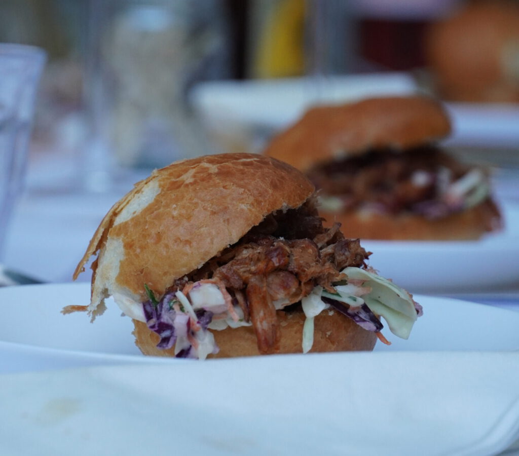 Zacht broodje gevuld met langzaam gegaard pulled pork, geserveerd in een warme, huiselijke BBQ‑setting.